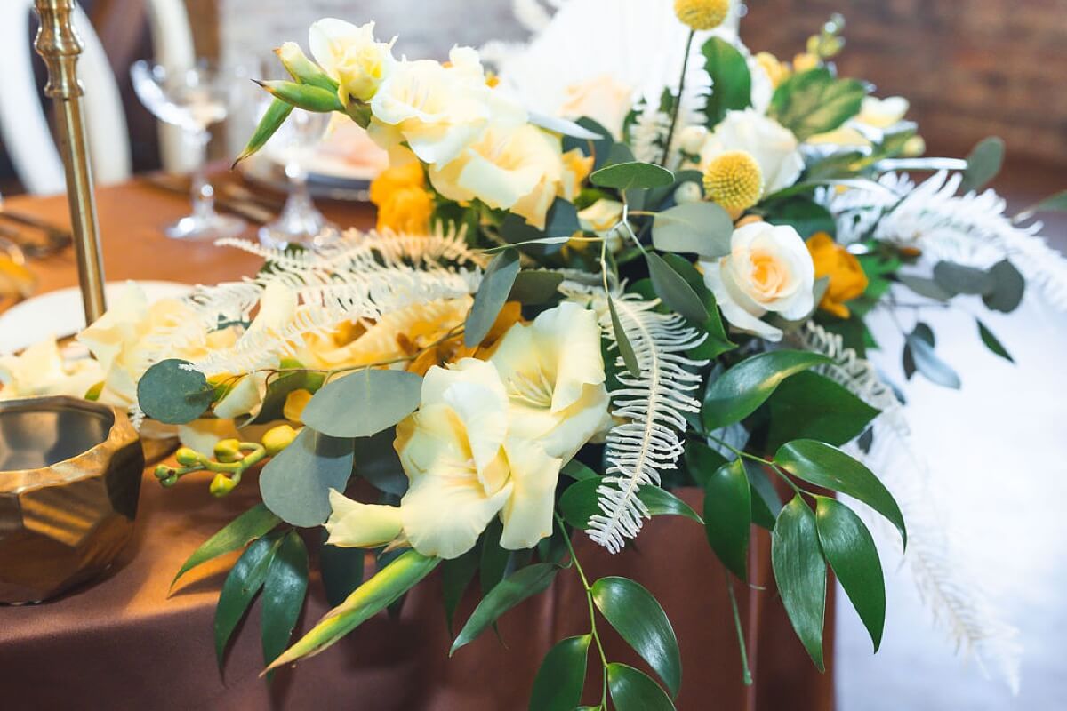 White and yellow flowers with greenery at golden inspired styled shoot