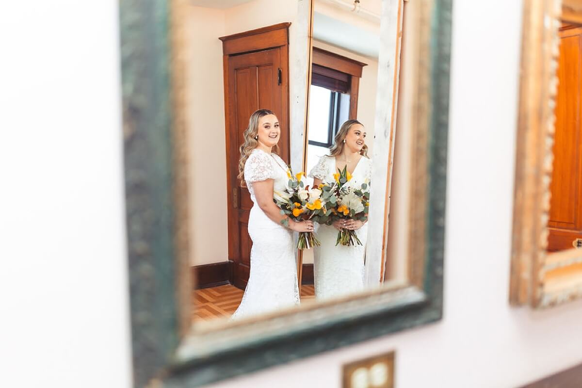 Bride holding bouquet and looking in mirror at loft wedding venue Chicago