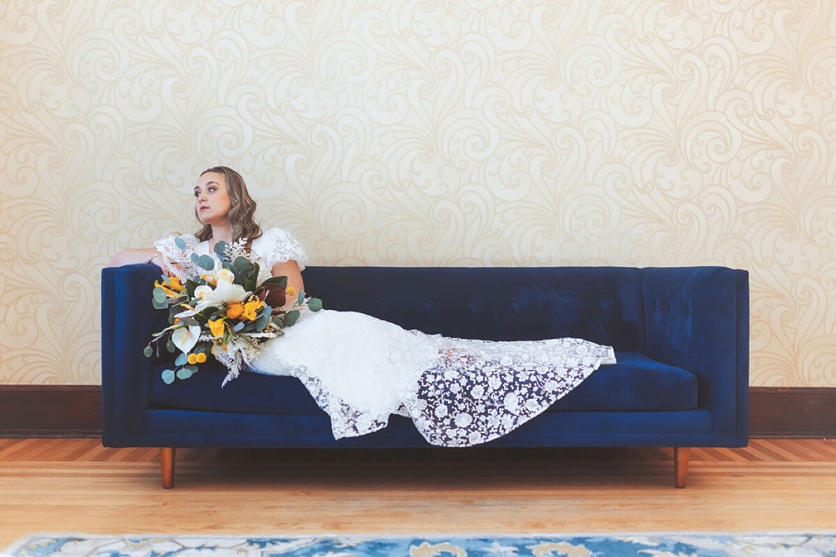 Bride sitting on blue velvet couch while holding bouquet at loft wedding venue Chicago