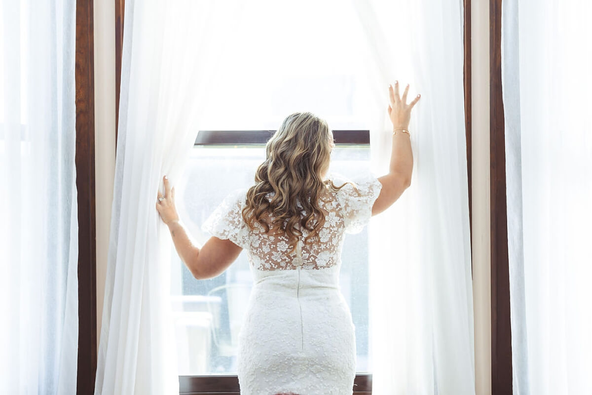 Bride with lace back wedding dress standing in window