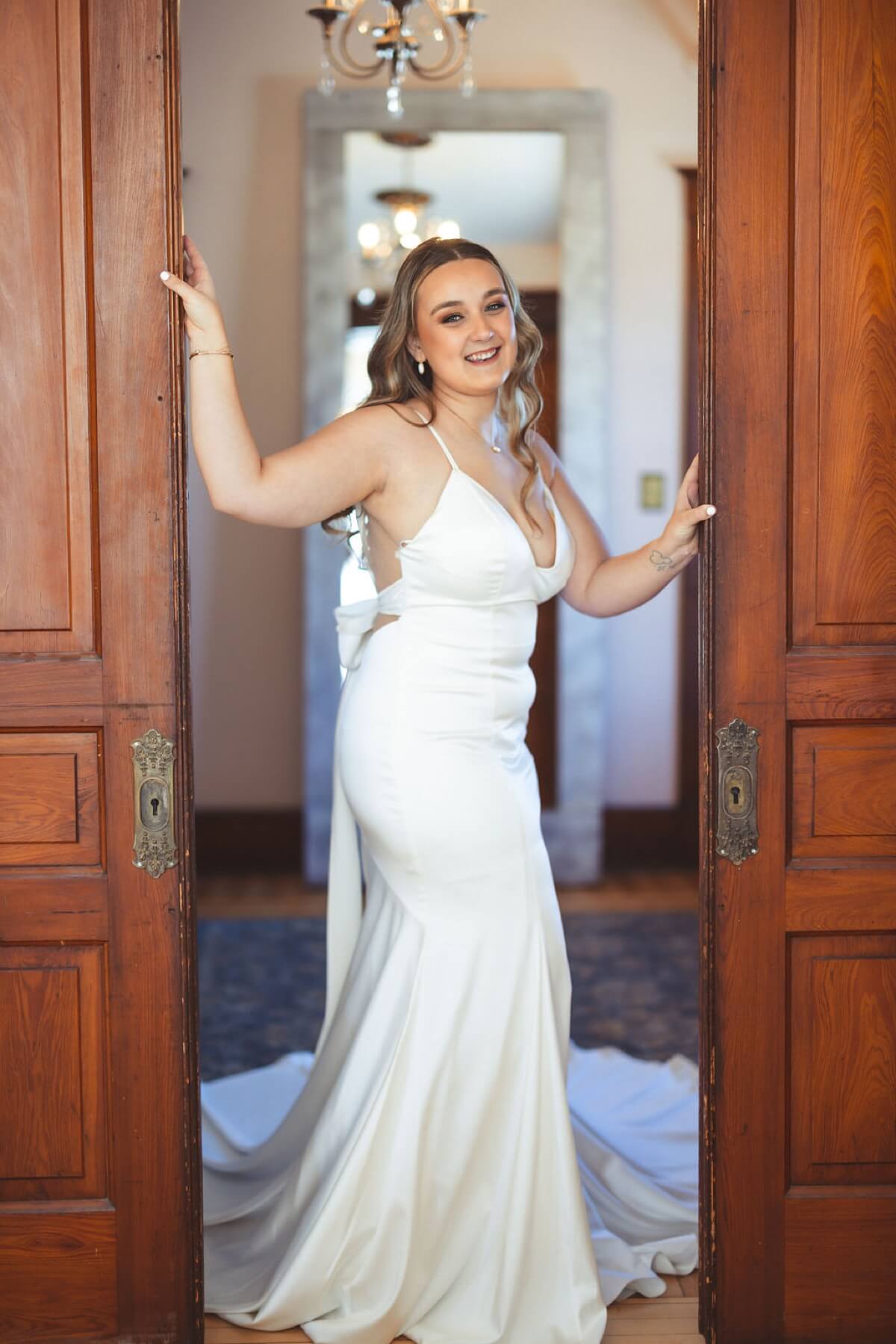 Bride wearing satin wedding dress standing in between wooden sliding doors