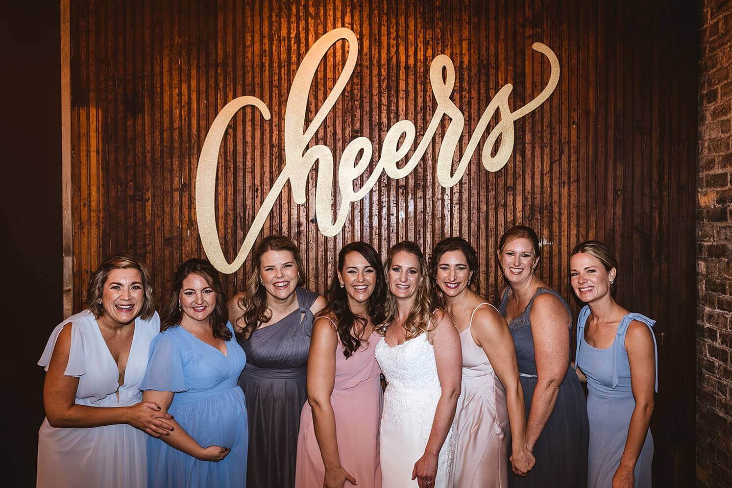 Bride with bridesmaids in front of the cheers sign at The Haight, a winter wedding venue