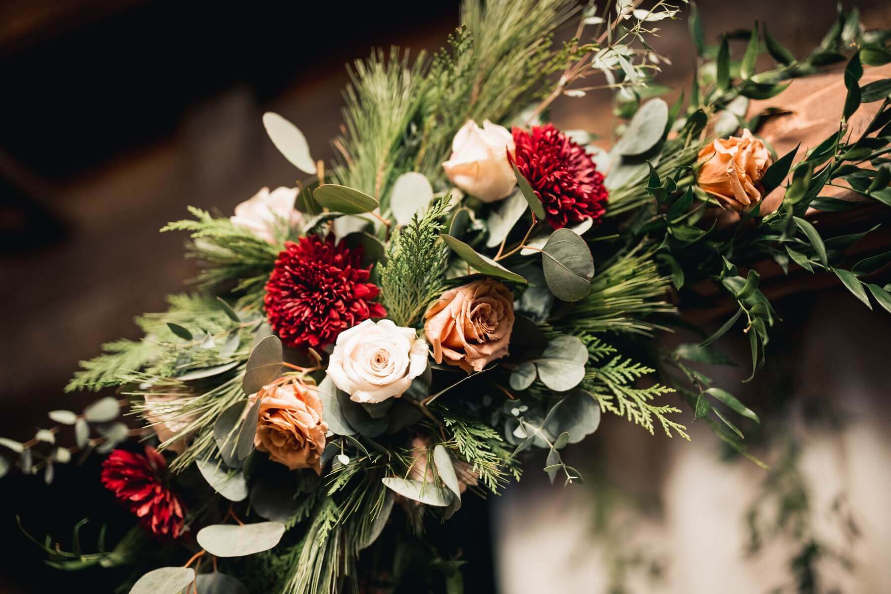 white, peach, and crimson flowers with greenery on arch