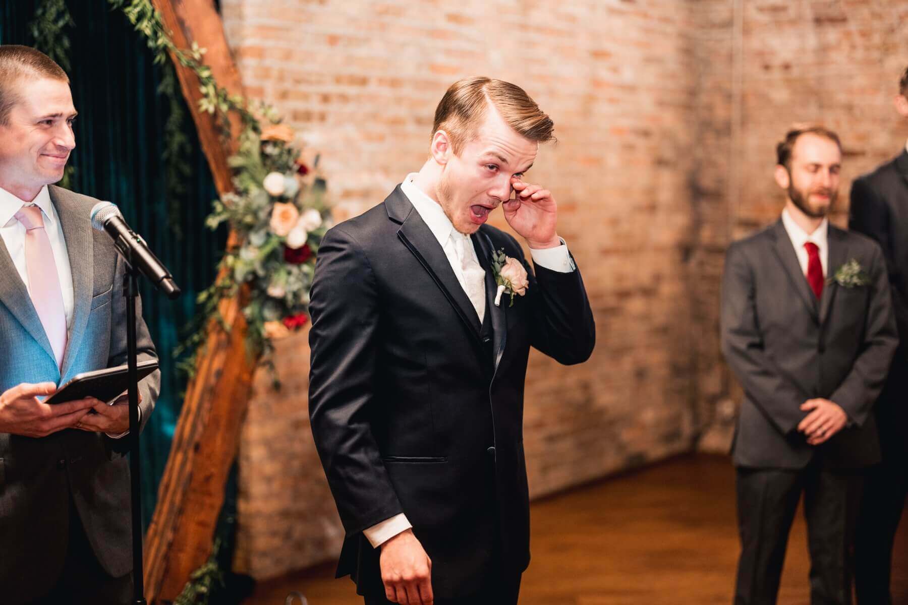 Groom wiping tears from his eyes as bride walks down the aisle