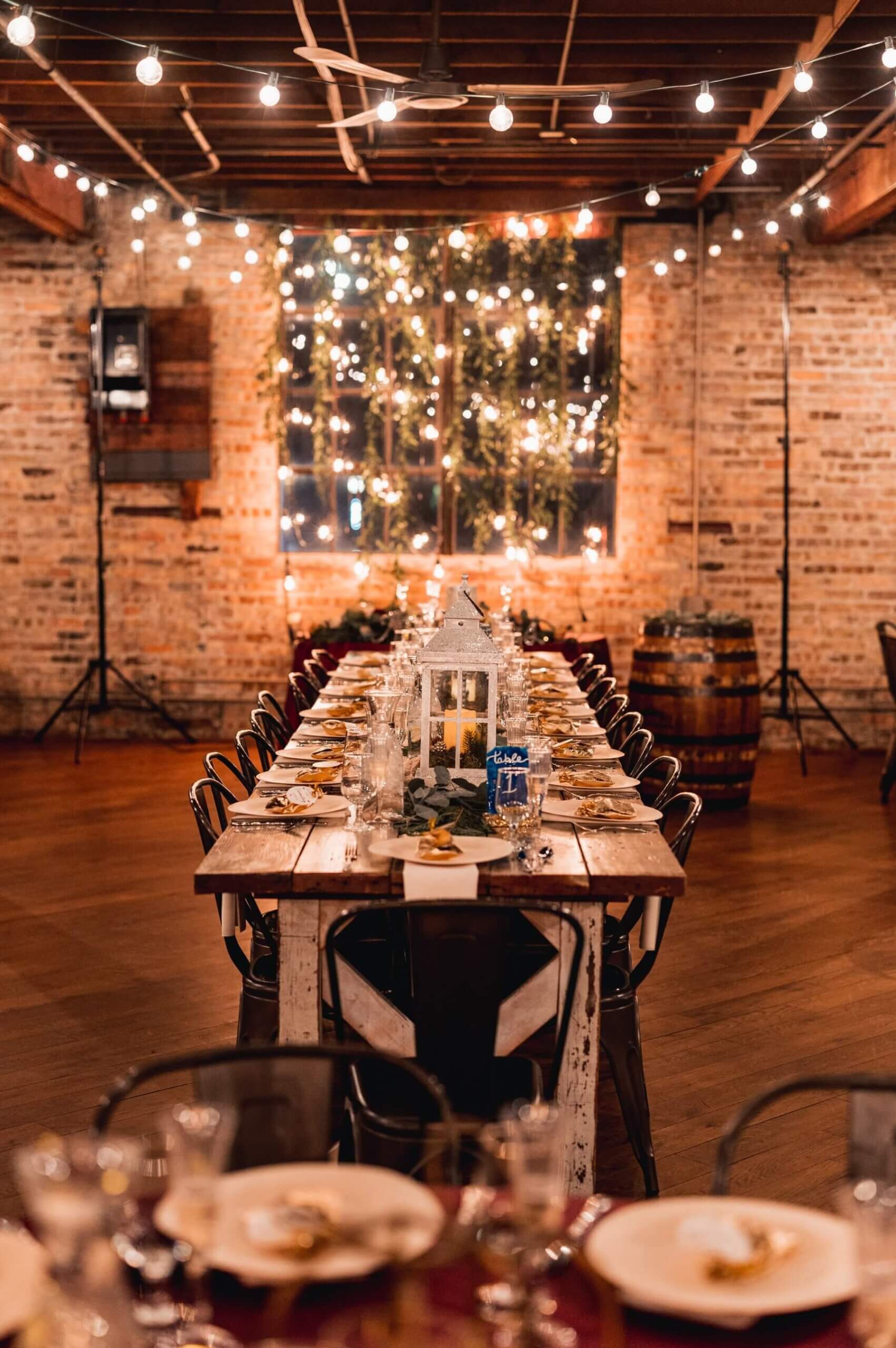 Farm table with lanterns with wall of greenery and lights at wedding venue in Illinois