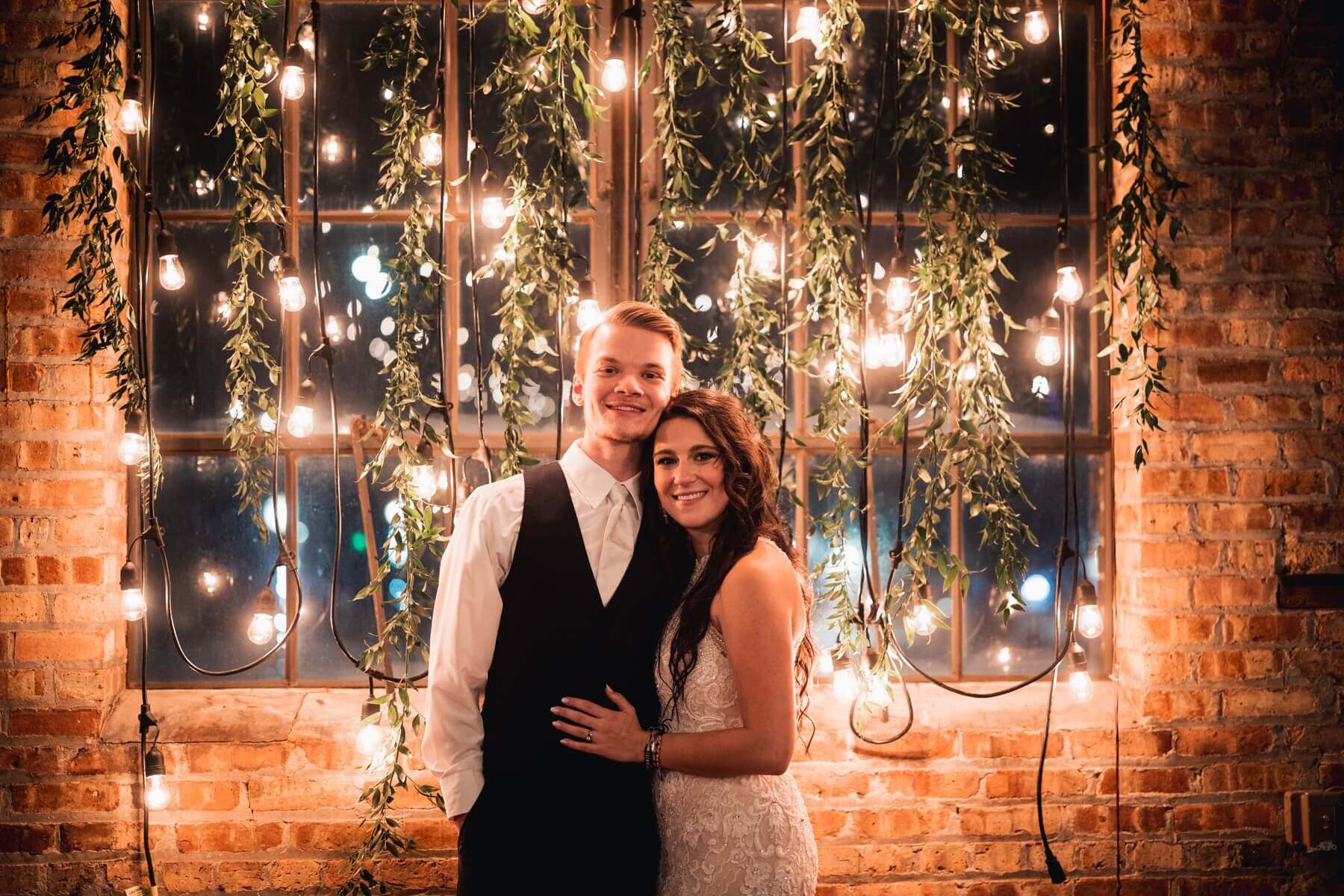 Bride and groom standing in front of greenery and twinkle lights at The Haight