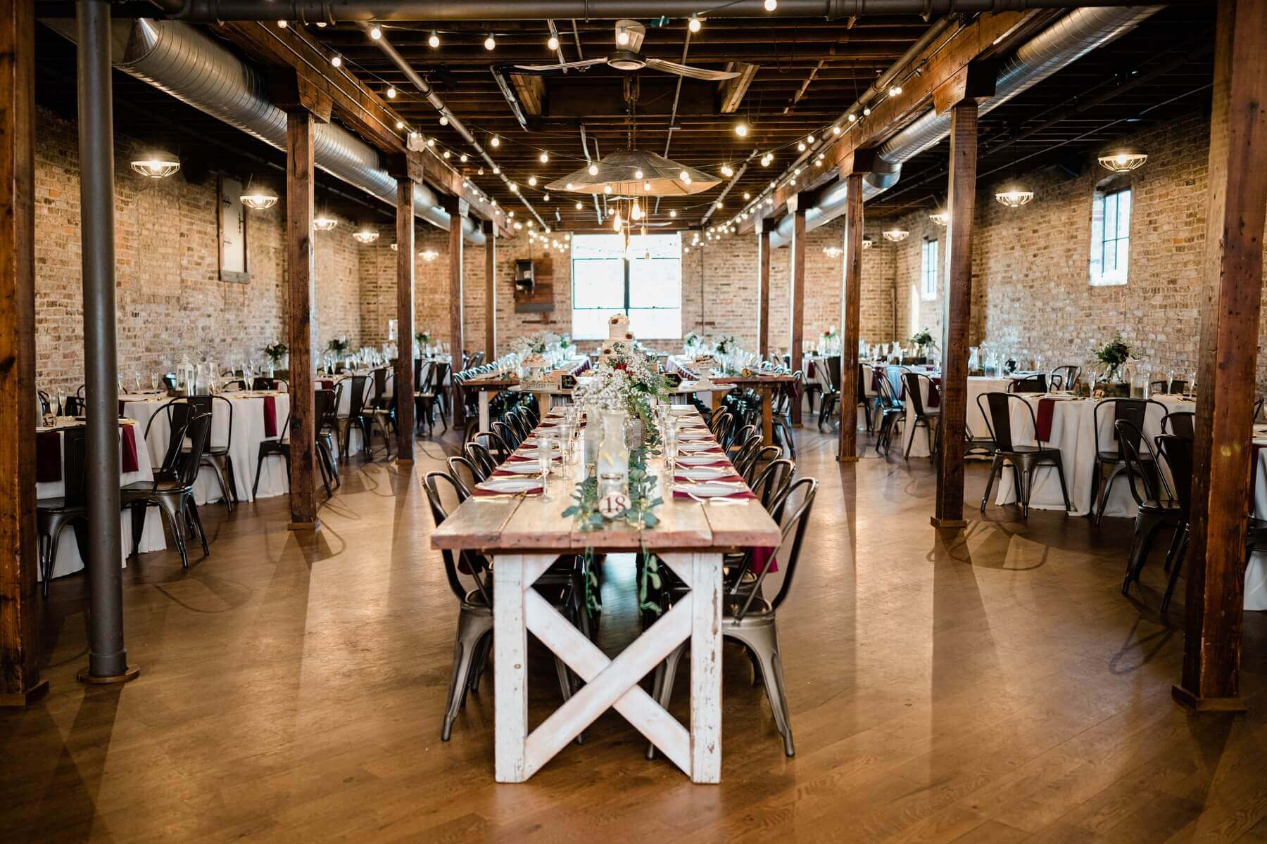 Rustic wedding reception including farmhouse tables, metal chairs, and rustic wood boxes with red and white flowers