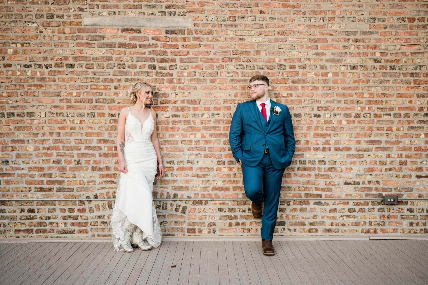 Bride and groom leaning against brick wall and looking at each other