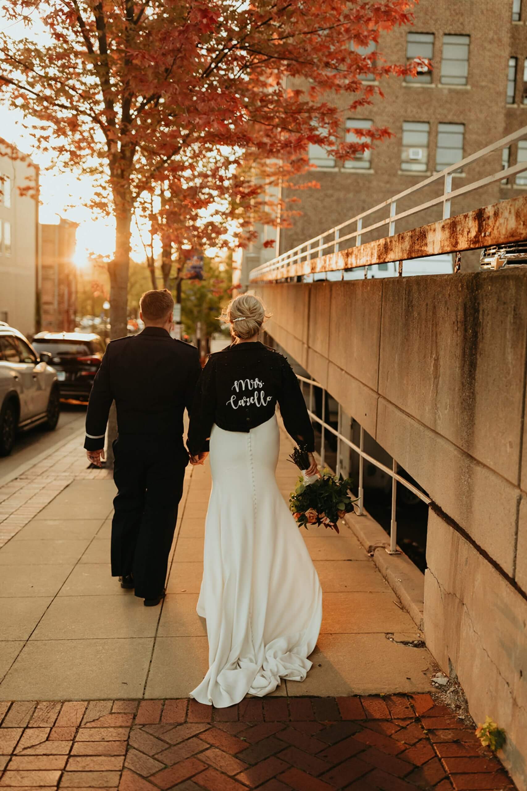 Bride wearing black jacket with her married name walking with groom