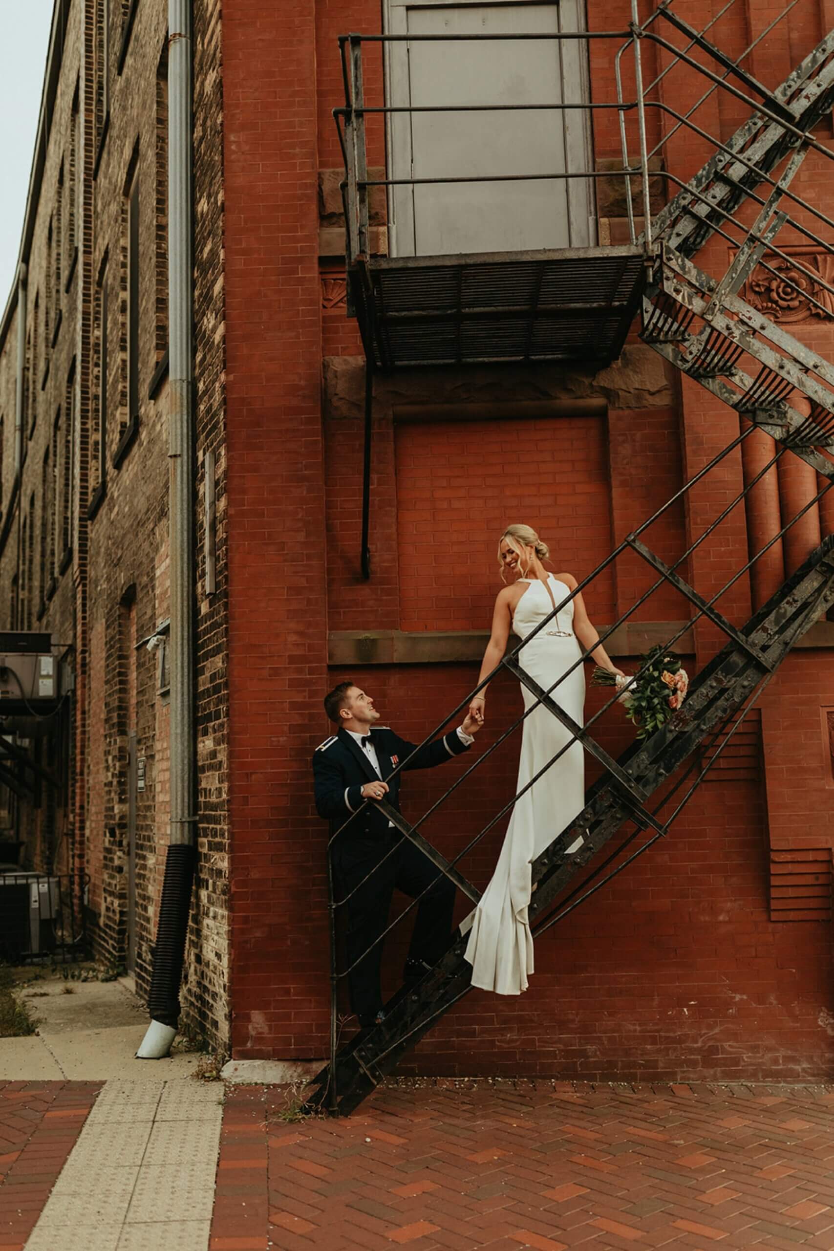 Bride standing on stairs on outside of building looking down at groom