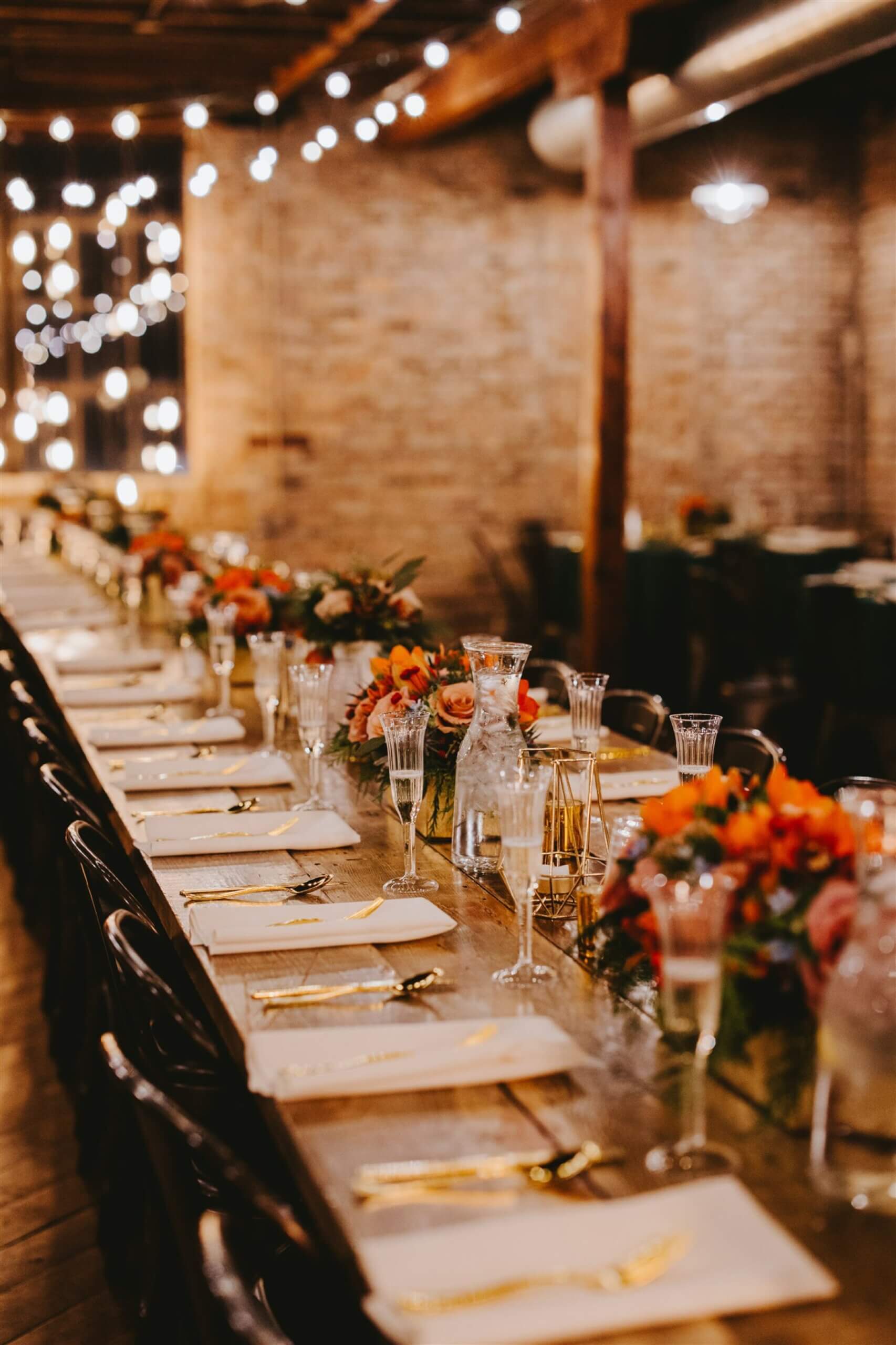 Wedding reception table with gold accents and red, pink, and orange flowers
