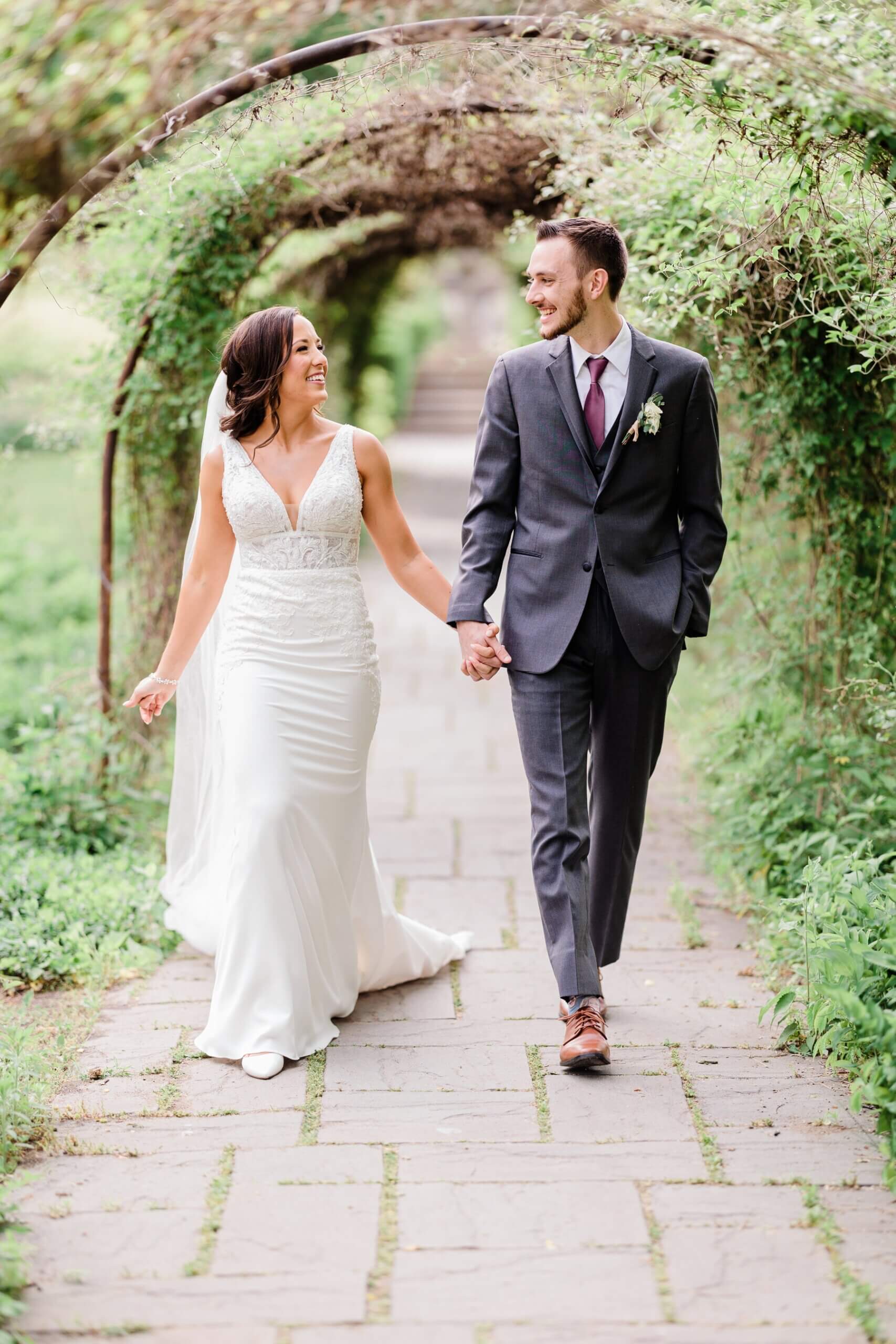 Bride and groom holding hands and walking under ivy covered arches