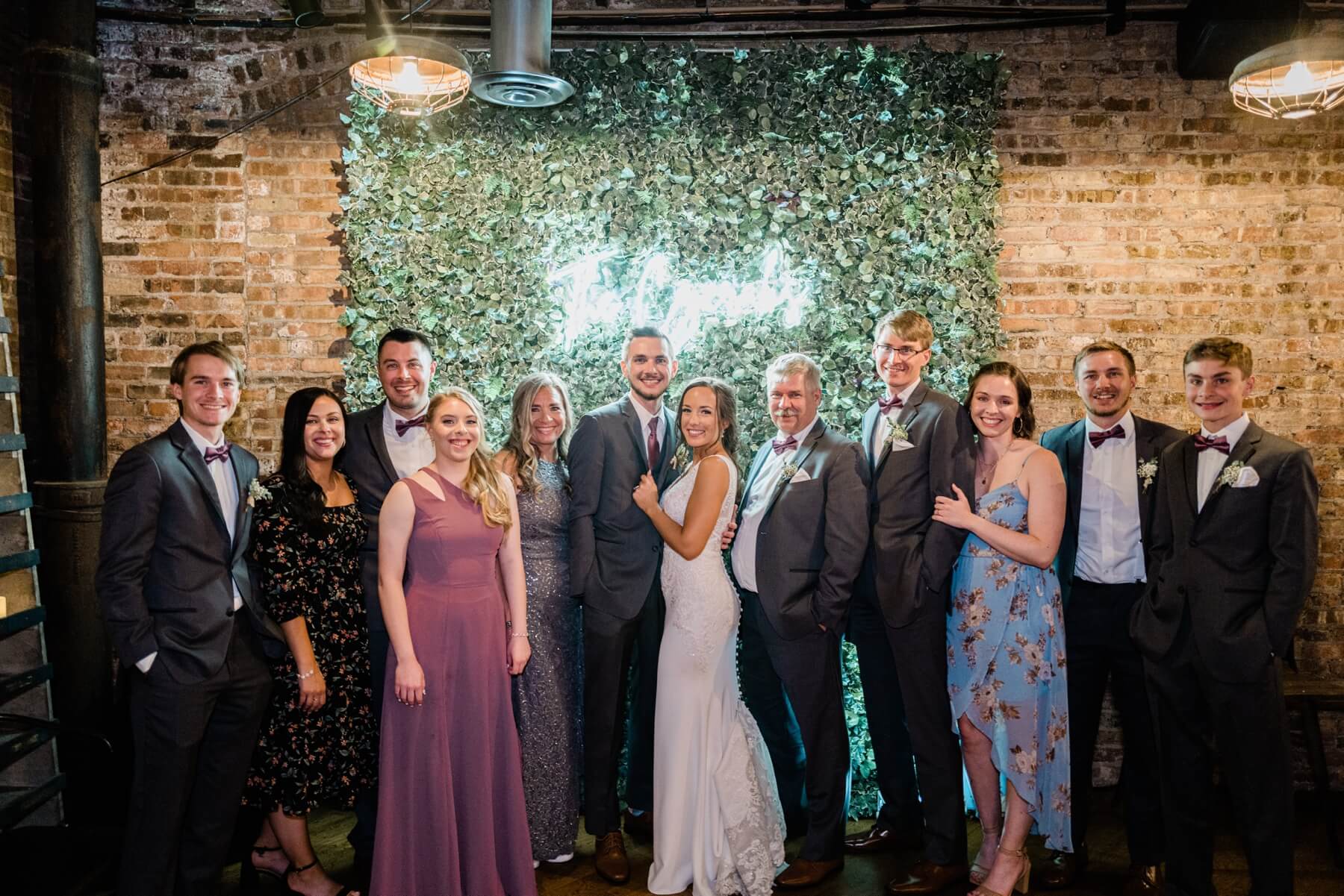 Bride and groom and their family standing in front of ivy wall with neon sign