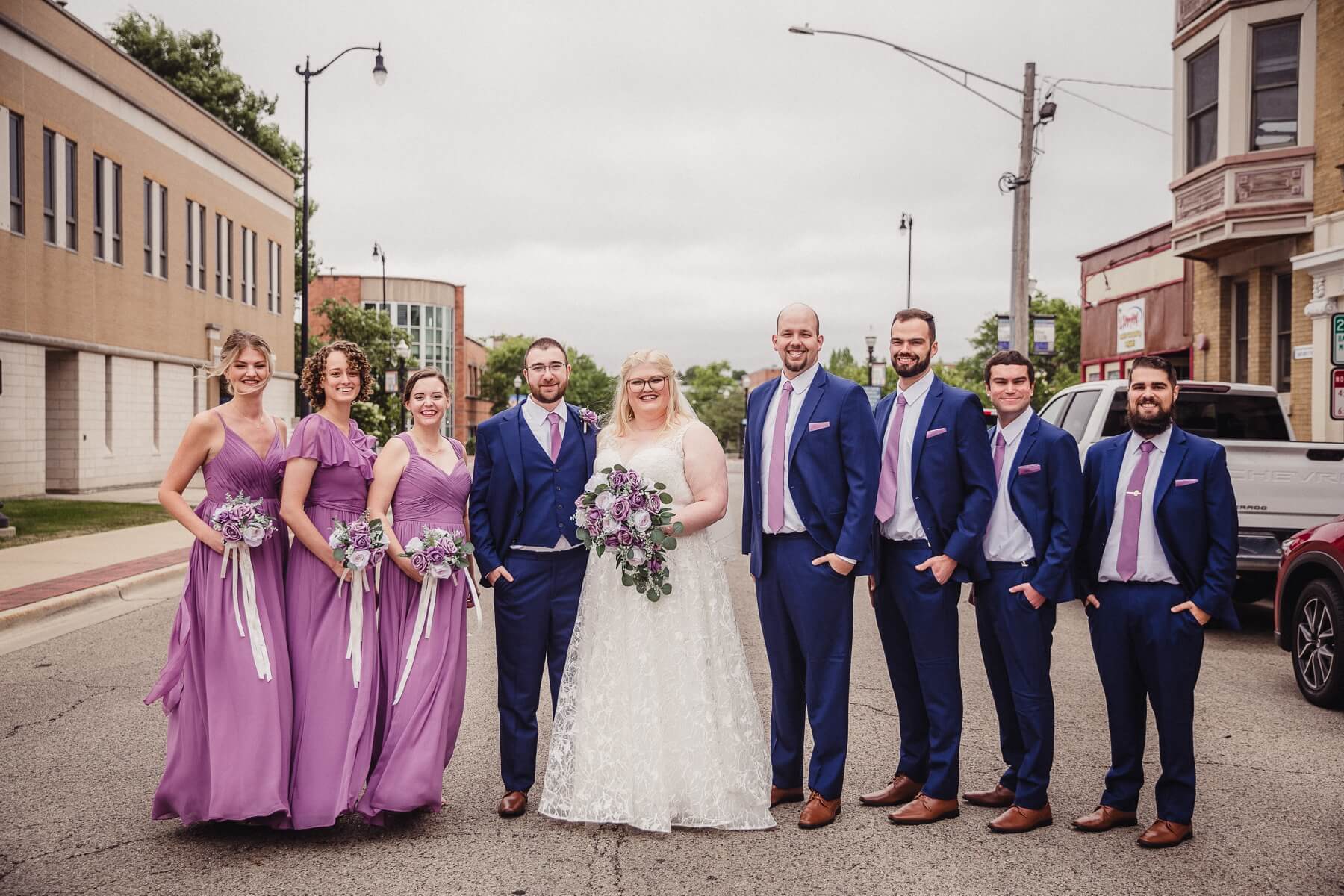 Bride and groom with bridesmaids in purple dresses and groomsmen in blue suits