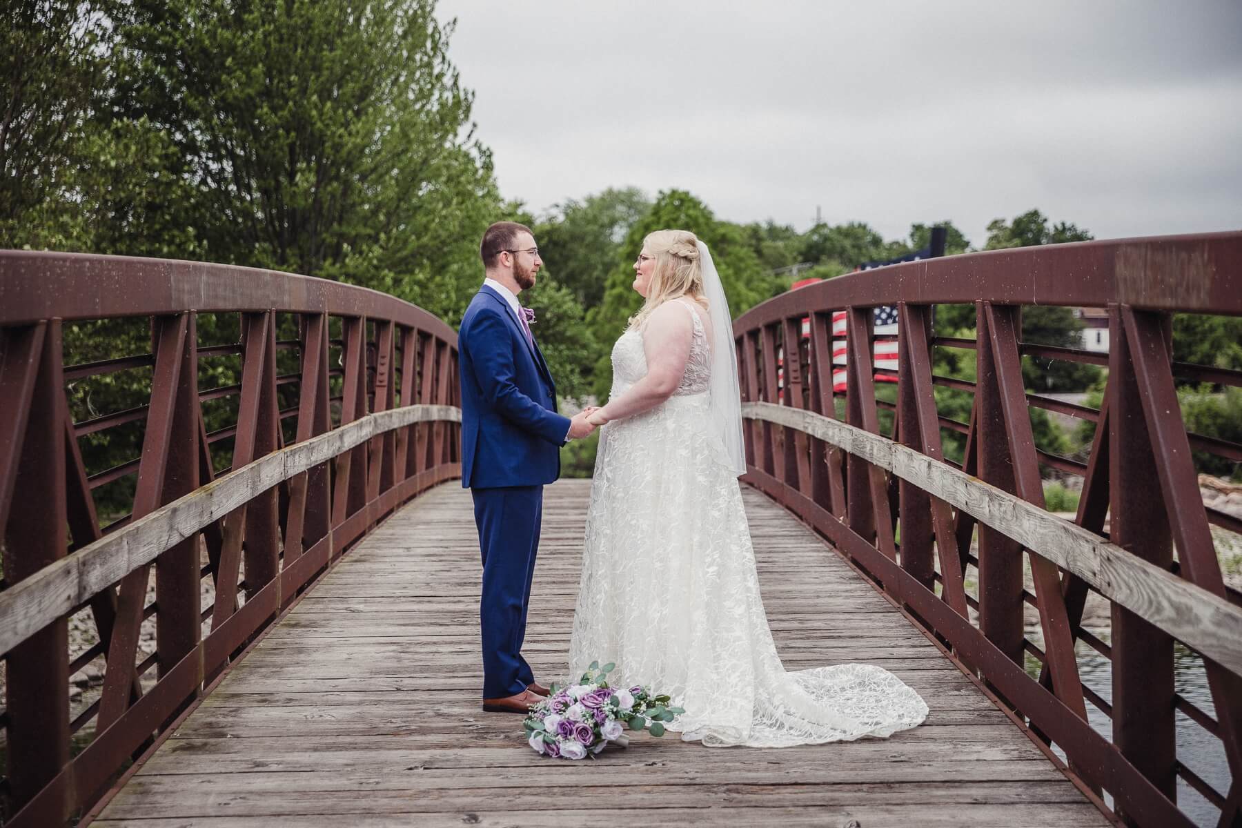 Bride and groom holding hands and looking at each other while standing on bridge