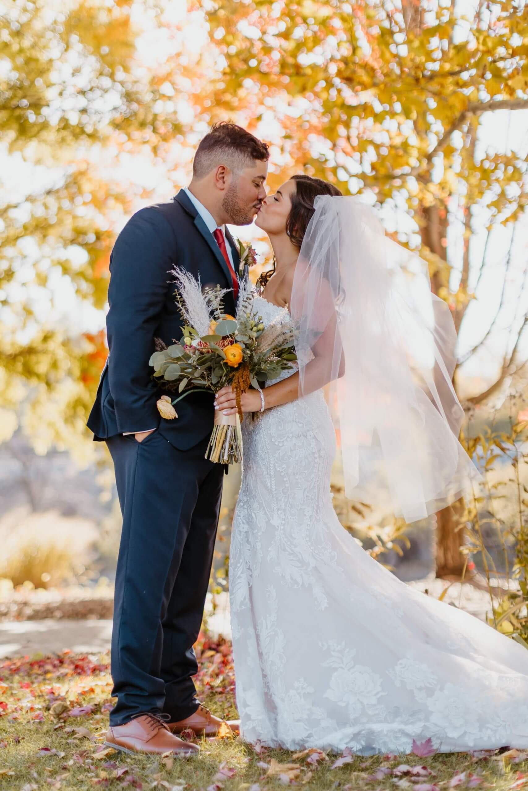 Bride and groom kissing while standing under fall trees
