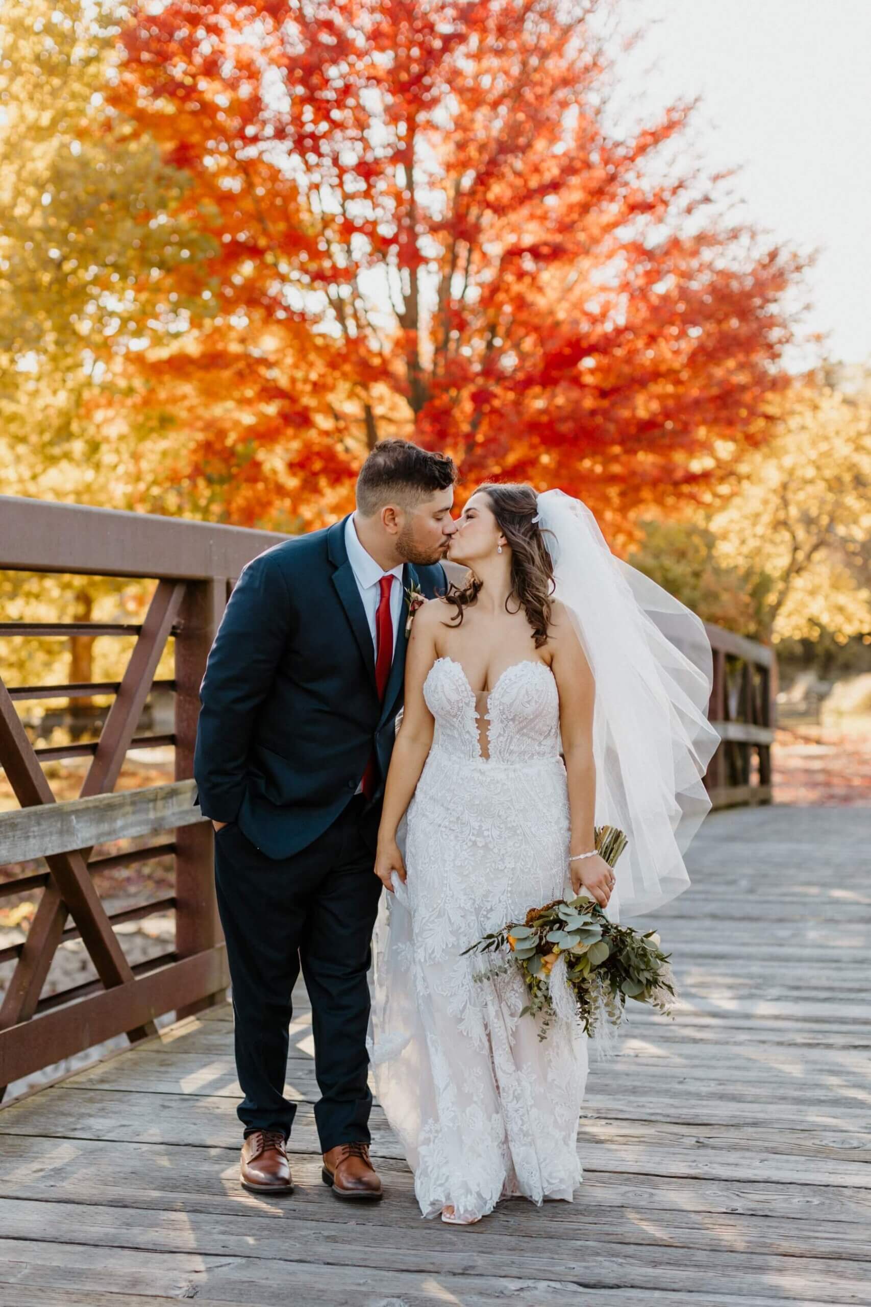 Bride and groom kissing on bridge with fall trees in the background