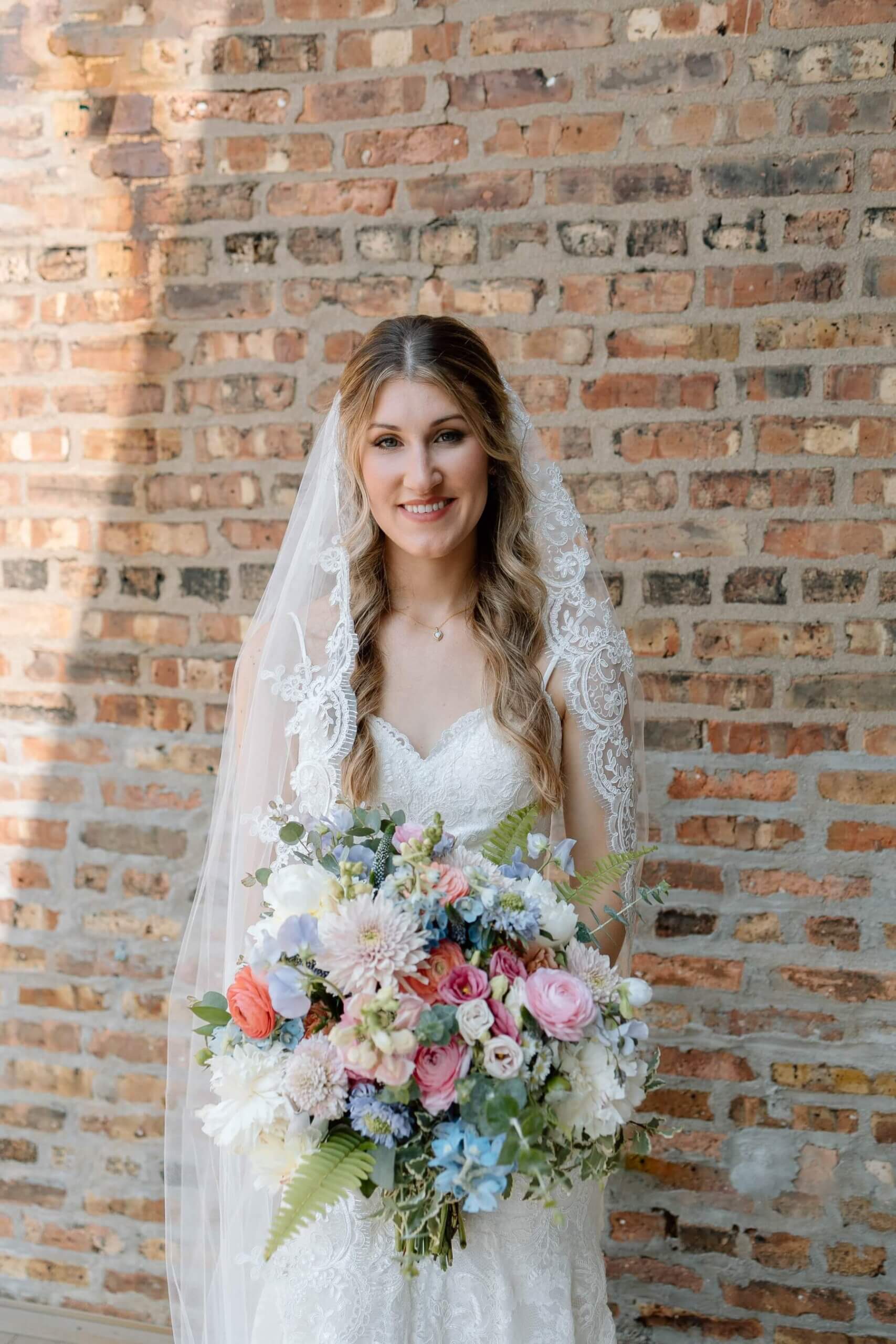 Bride wearing lace gown with lace veil holding colorful summer bouquet