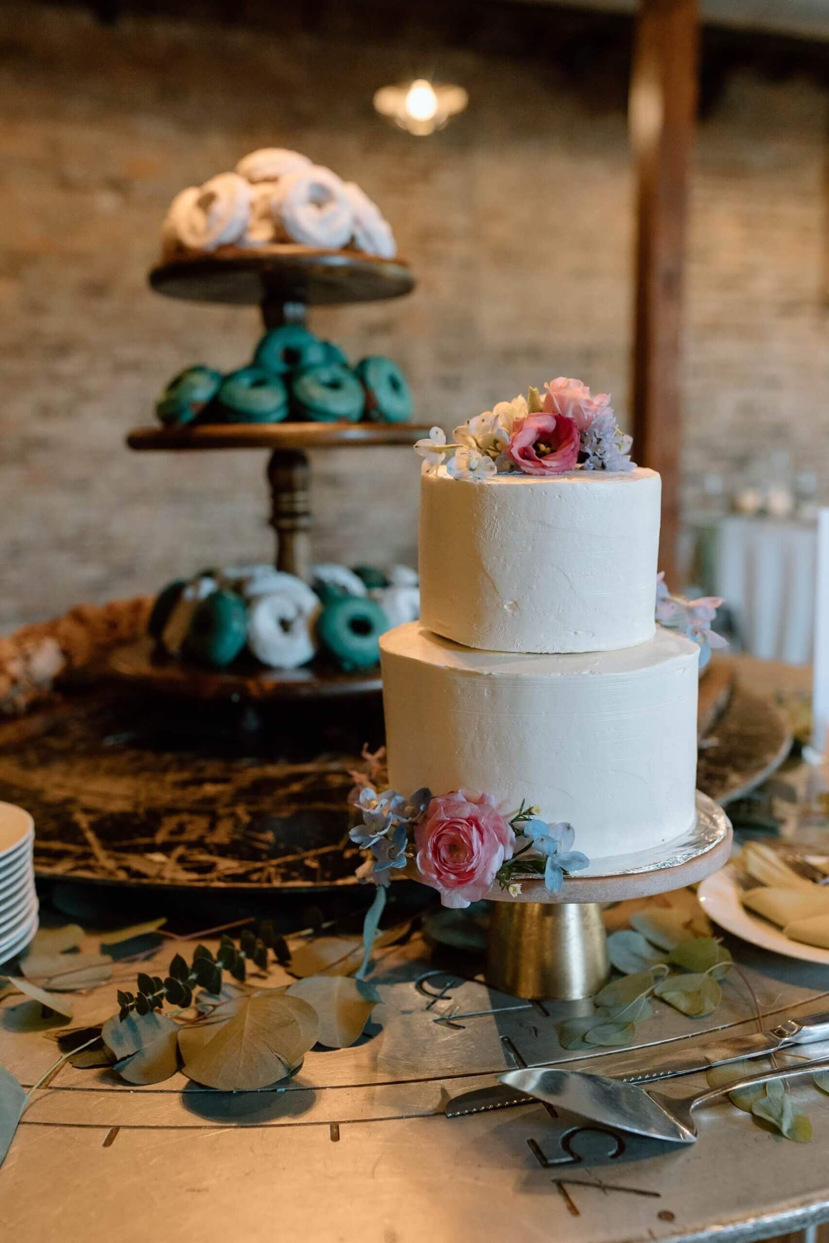Two tier white wedding cake with flowers and donuts on table